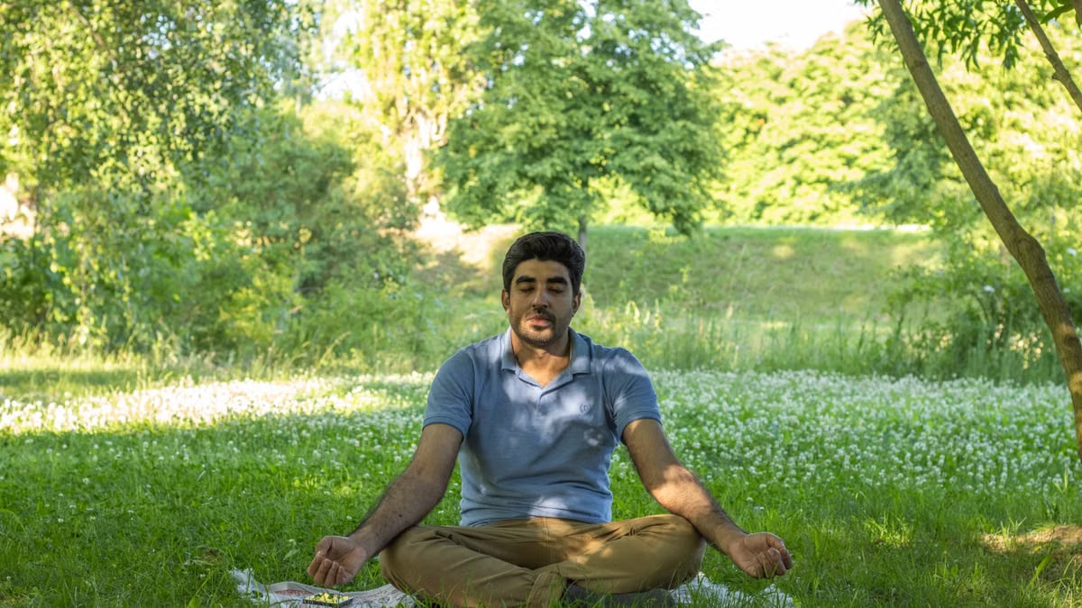 Man practicing meditation in a peaceful park, surrounded by nature, promoting wellness and inner peace.